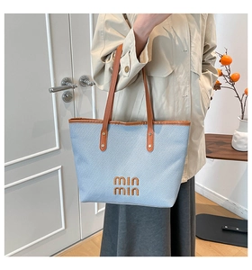 Close-up of light blue textured tote bag with brown leather handles and orange embroidery