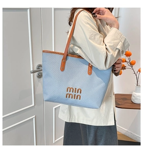 Detail of blue woven fabric tote bag with brown leather handles and stitched logo