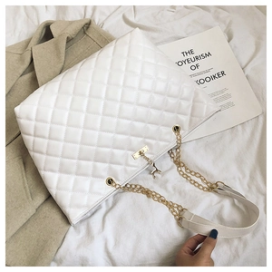 Detail of white quilted tote bag with gold chain strap and deer charm on fabric