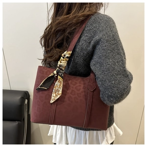 Macro view of burgundy suede tote bag with leopard texture and decorative silk scarf wrap