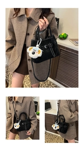 Detail view of black suede handbag with contrast stitching and plush puppy charm