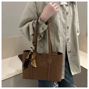 Detail of leopard print tote bag with decorative silk scarf handle on brown suede