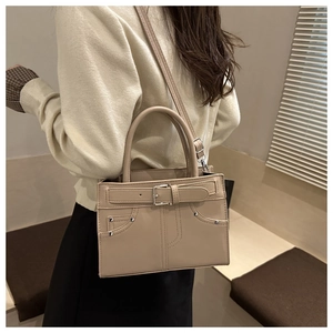 Close-up of beige crossbody bag with decorative silver rivets and metal buckle detail