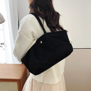 Sac fourre-tout minimaliste en daim noir mat avec boucles dorées porté par un mannequin
