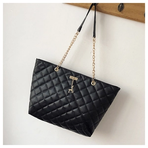 Detail of black quilted tote bag featuring golden deer charm and metal chain strap