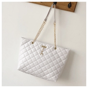 Close-up of white quilted tote bag featuring a gold deer charm and chain strap detail