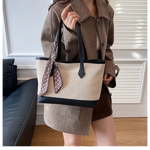 Detail of beige canvas tote with black leather trim and decorative lettered silk scarf