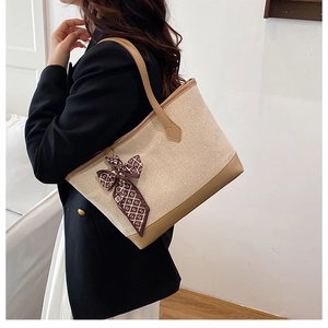 Detailed side view of canvas tote bag with leather trim and decorative silk scarf accessory