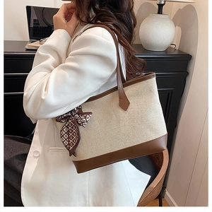 Beige canvas tote bag with brown leather trim and silk scarf in an office setting