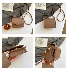 Detail der braunen Ledertasche mit Narbenstruktur, Goldbeschlag und Plüschmonster-Anhänger