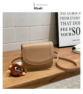 Detail of khaki lychee grain leather handbag with a brown plush monster charm on wood
