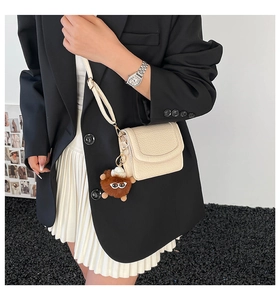 Detail of off-white lychee grain leather crossbody bag with brown plush pendant
