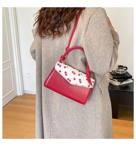 Detail view of a small square handbag with cherry print and red leather on model's outfit