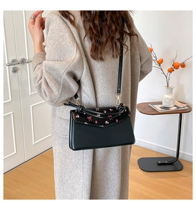 Model wearing a black leather crossbody bag with pink floral and bow embroidery detail