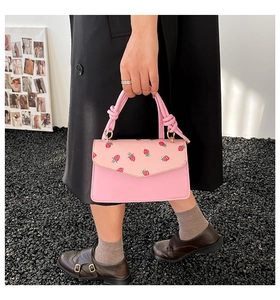 Detail of sweet pink handbag featuring strawberry print and unique knotted handle design