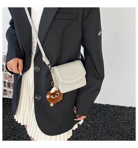 Close-up of creamy white lychee grain crossbody bag with cute brown plush monster charm