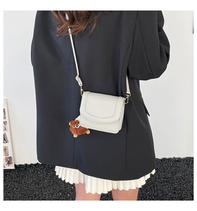 Model trägt minimalistische cremeweiße Satteltasche aus Leder mit Plüschanhänger-Detail