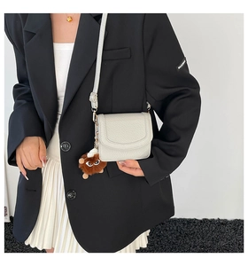 Close-up of a white lychee grain crossbody bag with a playful brown plush pom-pom charm