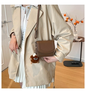 Brown litchi pattern leather crossbody bag with cute plush pendant on a stylish model