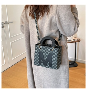 Detail of crossbody bag with M letter print and black strap shown on a model