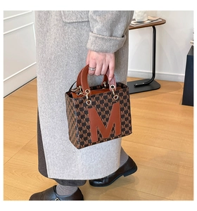 Close-up of brown tote bag with repeating M-letter print and structured leather handle