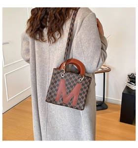 Detailed close-up of embroidered handbag with letter pattern and brown leather handle