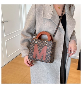 Detail of vintage patterned handbag with M logo on a model in a long wool coat