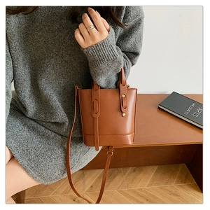 Brown leather bucket bag styled as a shoulder bag on a model in a minimal setting