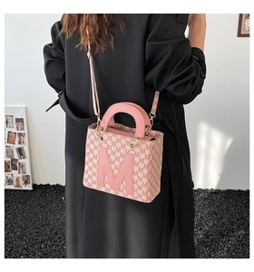 Détail du sac cabas rose avec motif M porté par un mannequin en manteau noir