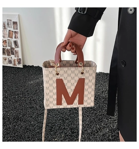 Detail of cream tote bag with grey monogram pattern and brown leather M applique