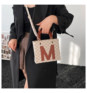 Detail of crossbody tote bag with M-pattern print and brown leather handles