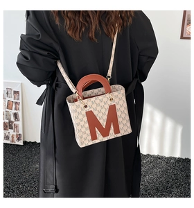 Modern beige tote bag with M-letter monogram and brown leather handles shown on model