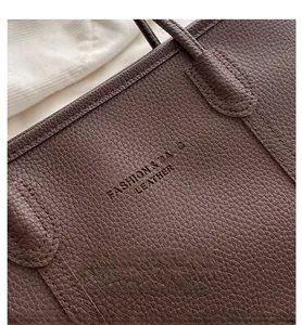 Macro shot of brown lychee grain leather tote bag with embossed fashion text detail