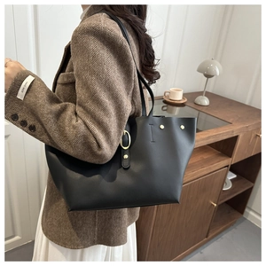 Dettaglio di una borsa tote nera con fibbie dorate indossata su un blazer di lana