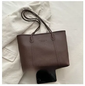 Detail of dark brown pebble leather tote bag with logo and smartphone for size scale