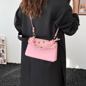 Pink heart shoulder bag with strawberry print and knotted handle on black coat model
