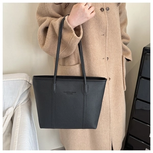 Detail of black pebbled leather tote bag with embossed logo and long shoulder straps