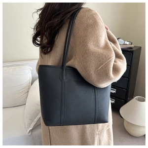 Detail of a black pebbled leather tote bag with long straps on a camel wool coat