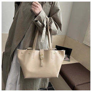 Dettaglio borsa tote beige con fibbia dorata e rivetti indossata con un trench kaki