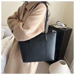 Detail of black pebbled leather tote bag with embossed logo worn with camel coat