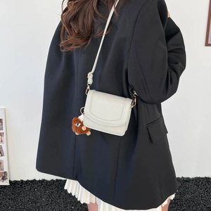 Minimalistische beige Umhängetasche mit Plüschbär-Anhänger an einem Model getragen