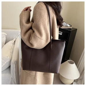 Close-up of a large dark brown lychee leather tote bag worn over the shoulder by a model