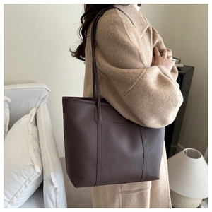 Detailed close-up of dark brown lychee-patterned leather tote with golden embossed text