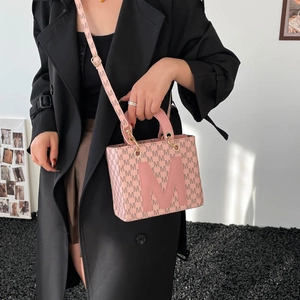 Sac à main rose avec broderie M et bandoulière sur mannequin dans un décor moderne chic