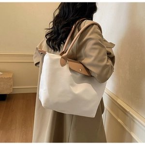 Detail of a large white nylon tote bag with khaki leather trim worn on the shoulder