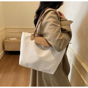 Close-up of a white tote bag with tan leather handles on a trench coat model
