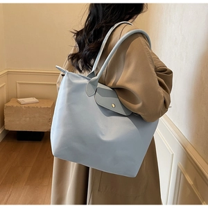 Spacious light blue nylon tote bag worn by a model in a minimalist stylish interior