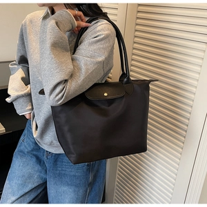 Minimalist black nylon tote bag with leather handles shown on shoulder for commuting