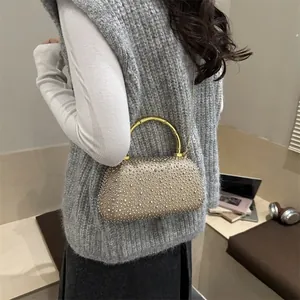 Elegante borsa da sera con strass, manico in bambù dorato e catena indossata da una modella