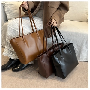 Tre borse tote grandi e minimaliste in pelle marrone e nera esposte su un divano